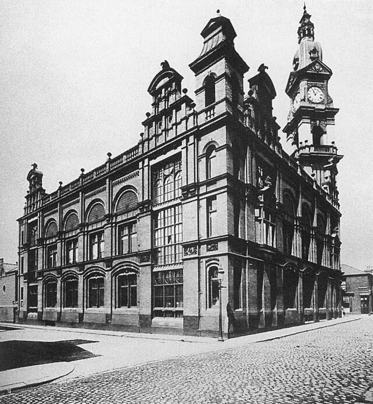 An old black-and-white photograph of a large building with a clock tower, taken from the outside